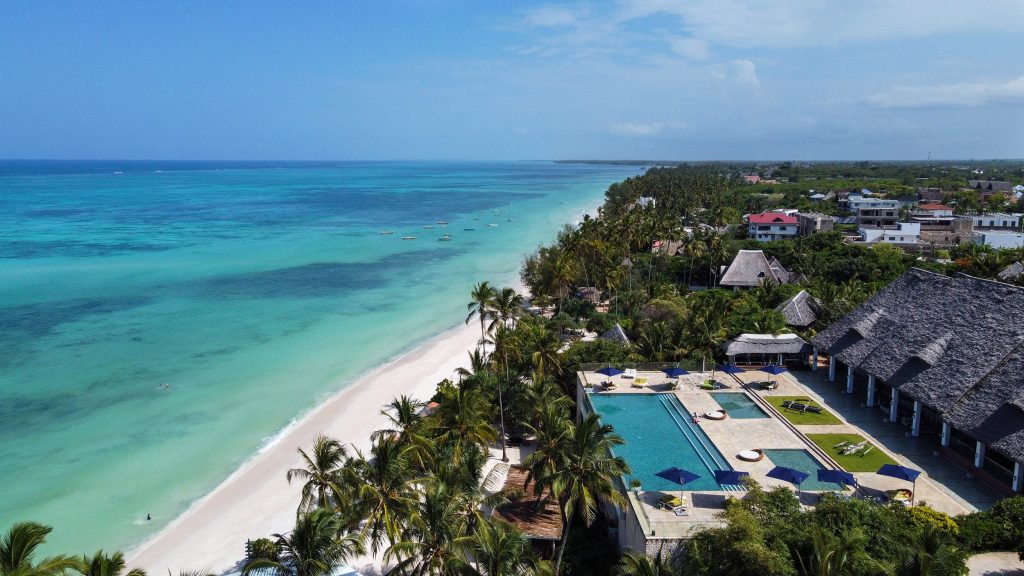 Luftaufnahme von Melia Zanzibar mit großem rechteckigem Pool, Strohdachgebäude, Palmen und hellem Sandstrand