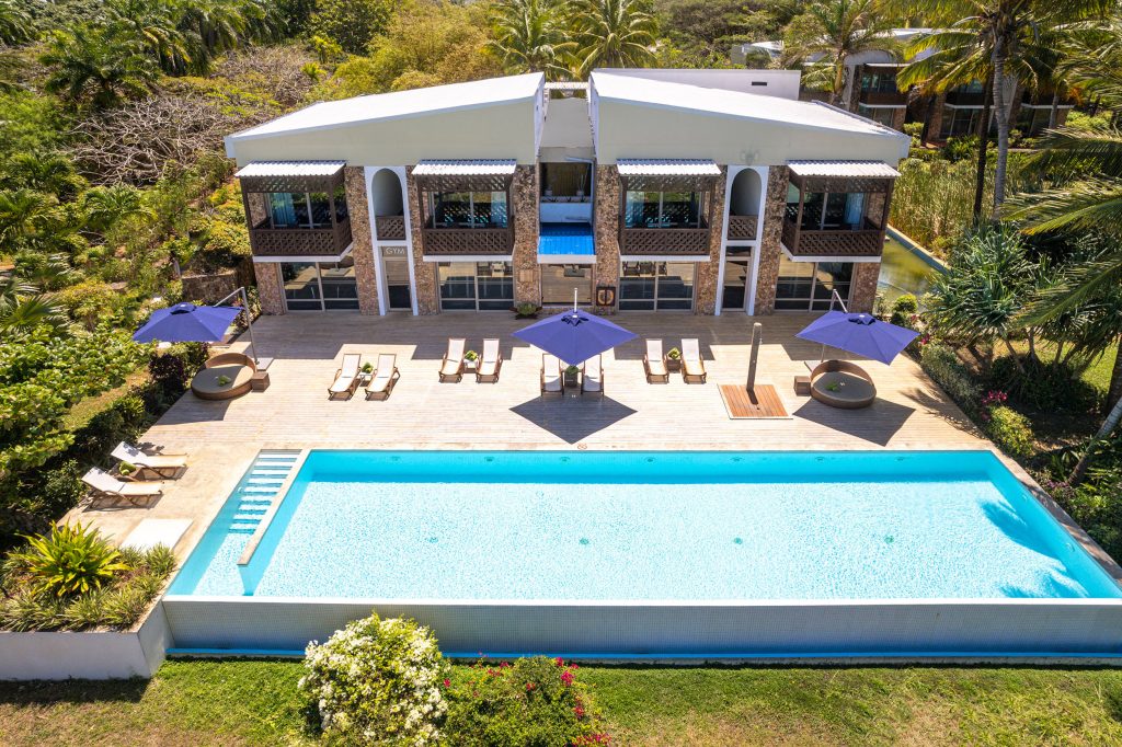 Vogelperspektive auf Melia Zanzibar mit rechteckigem Pool, Holzterrasse, Sonnenliegen und tropischer Vegetation