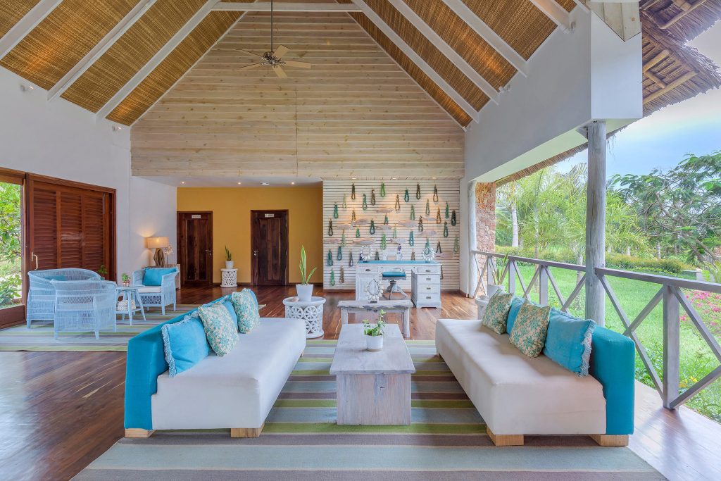 Offener Raum mit hohen Decken, zwei cremefarbene Sofas mit türkisfarbenen Kissen, Holzboden und Blick auf grüne Landschaft