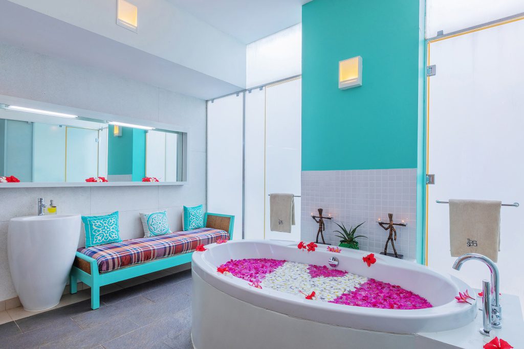Modernes Badezimmer mit großer ovaler Badewanne, farbigen Blütenblättern, weißen und türkisen Farbtönen, Glasfenstern