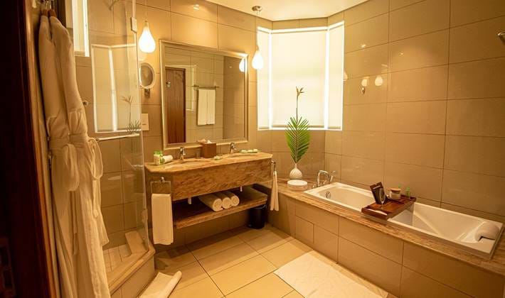Badezimmer im Sands Suites Resort & Spa mit Badewanne, Dusche mit Glaswand, beigen Fliesen und Waschbecken mit Spiegel