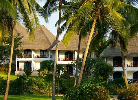Resort mit weißen Wänden, Reetdächern und Holzbalkonen umgeben von Palmen und grünen Gärten