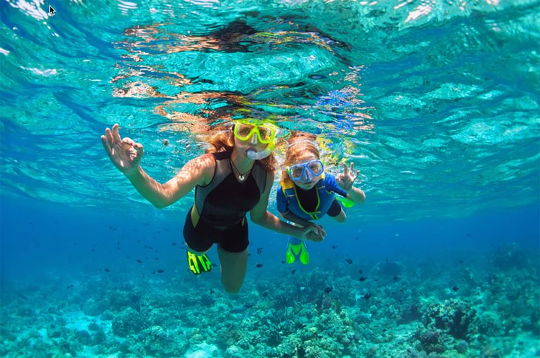 Familienurlaub auf Sansibar: Kinder spielen am ruhigen weißen Strand, Palmen im Hintergrund, türkisblaues Meer und sanfte Wellen.