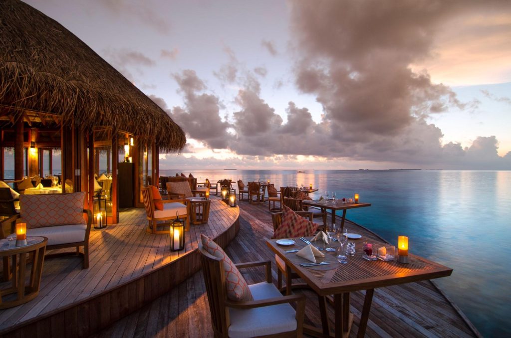 Restaurant auf Holzterrasse mit Holzmöbeln und Polsterkissen am ruhigen Ozean bei Dämmerung