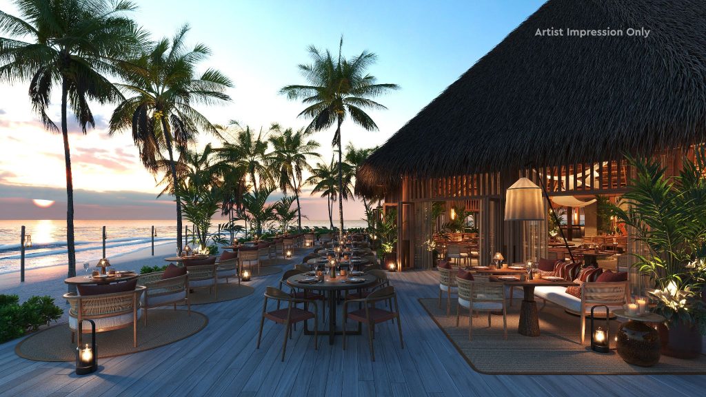 Außenansicht eines Strandrestaurants mit Holztischen und Stühlen auf Terrasse, Palmen im Hintergrund bei Sonnenuntergang