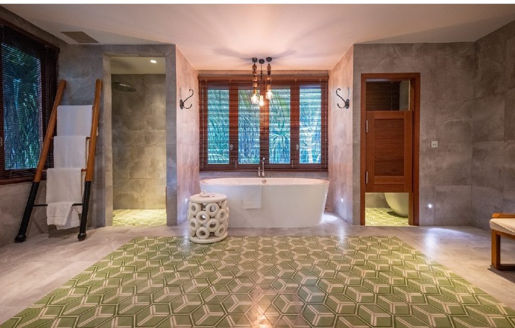 Badezimmer mit freistehender Badewanne, Holzleiter mit weißen Handtüchern, grün-weißer Fliesenboden und graue Steinwände
