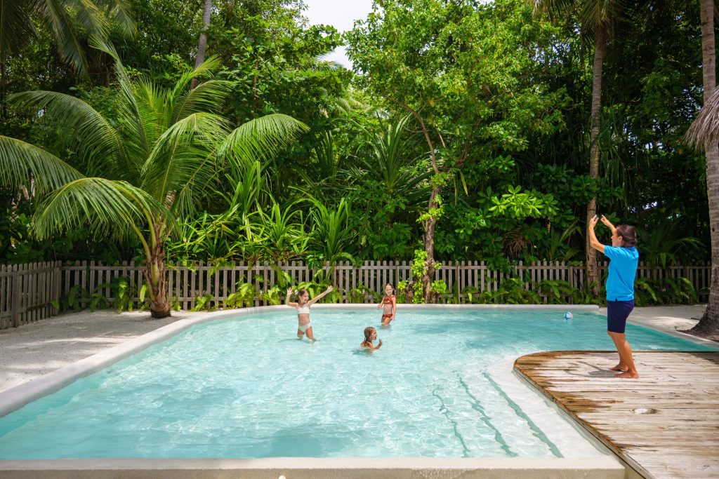 Rechteckiger Pool mit klarem Wasser, umgeben von Holzzaun und dichtem Grün, hölzernes Deck im Vordergrund