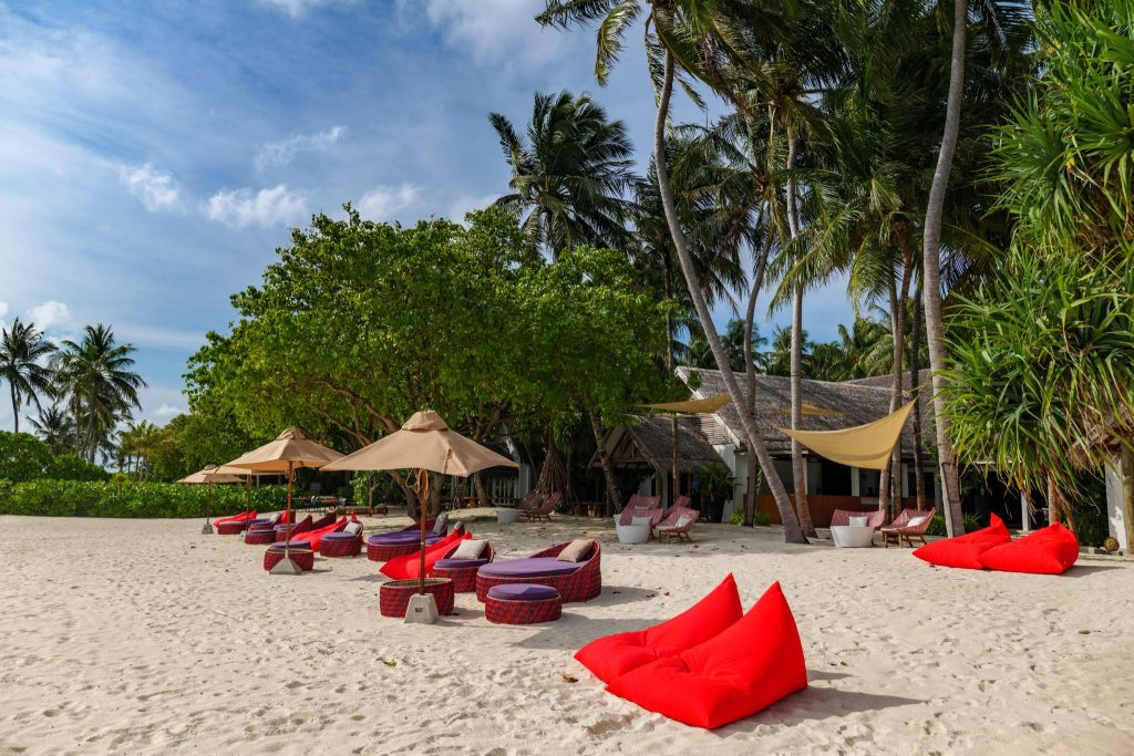 Strandabschnitt mit roten und violetten Sitzsäcken, rattanartigen Sitzgruppen und beigen Sonnenschirmen im Emperor Beach Club