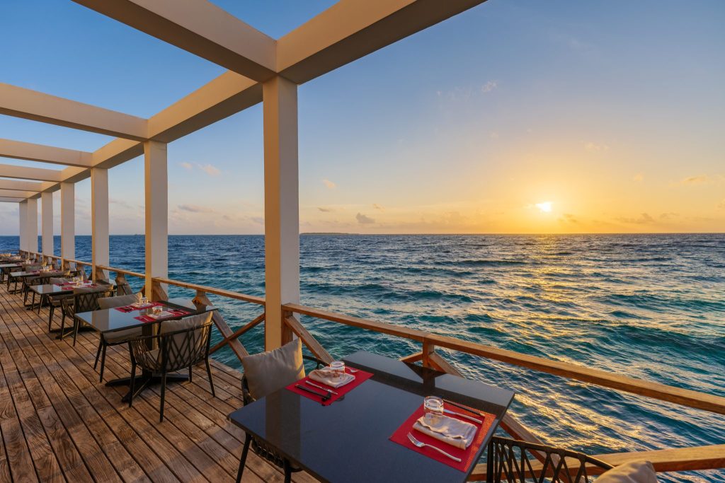 Terrasse des Restaurants feeling koi mit Holzboden, gedeckten Tischen und Blick auf Meer bei Sonnenuntergang