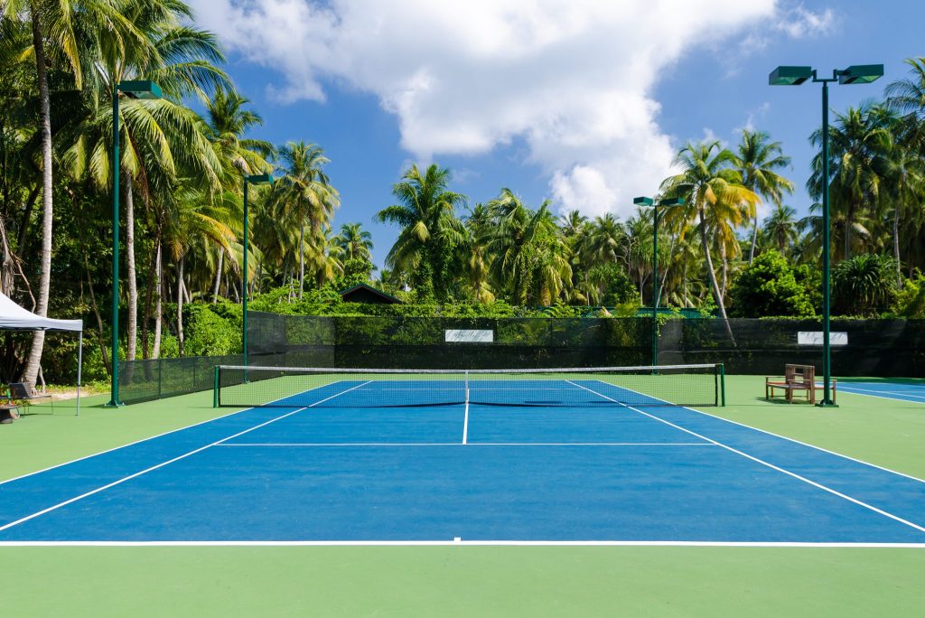 Tennisplatz mit blauem und grünem Hartbelag, umrahmt von Palmen und tropischer Vegetation auf den