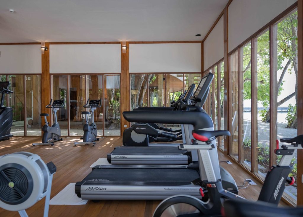 Moderner Fitnessraum im Amilla Maldives mit Laufbändern und Heimtrainern vor großen Glasfenstern zur grünen Außenlandschaft