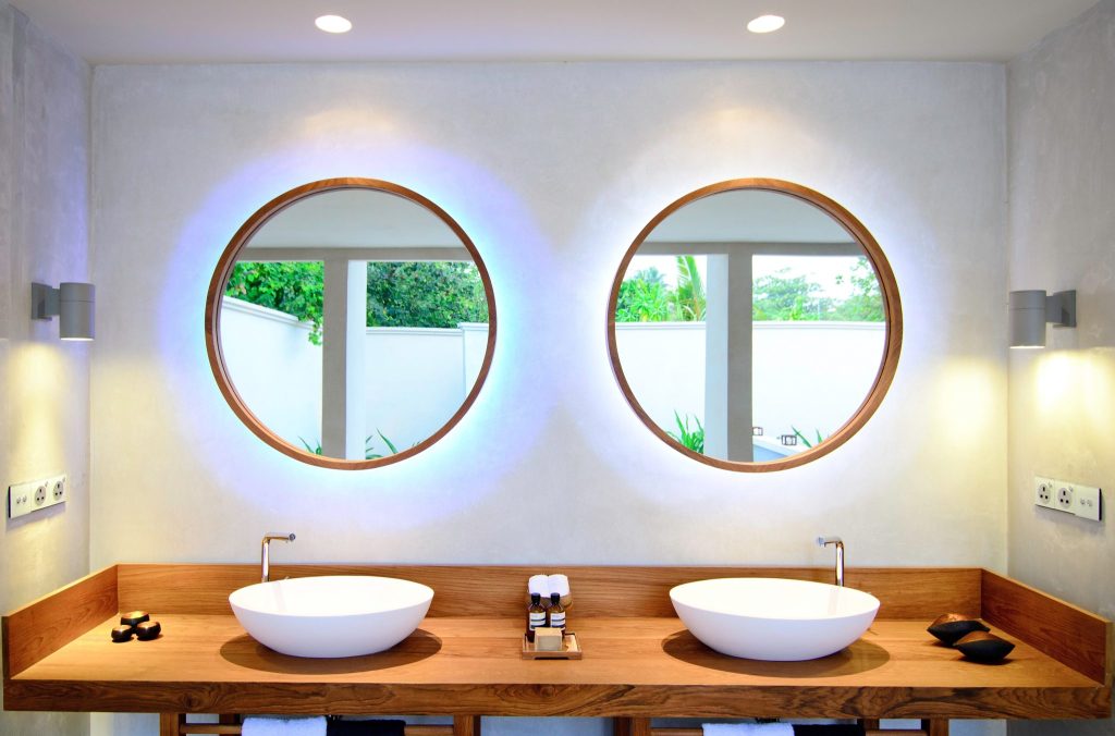 Modernes Badezimmer mit zwei runden Spiegeln, Doppelwaschbecken aus weißer Keramik, Holzplatte und natürlichem Licht