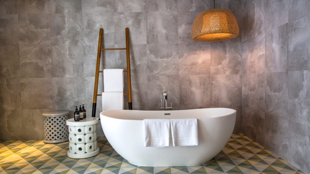 Badezimmer in Amilla Maldives mit weißer freistehender Badewanne, grauen Fliesen und bunter Bodenmusterung