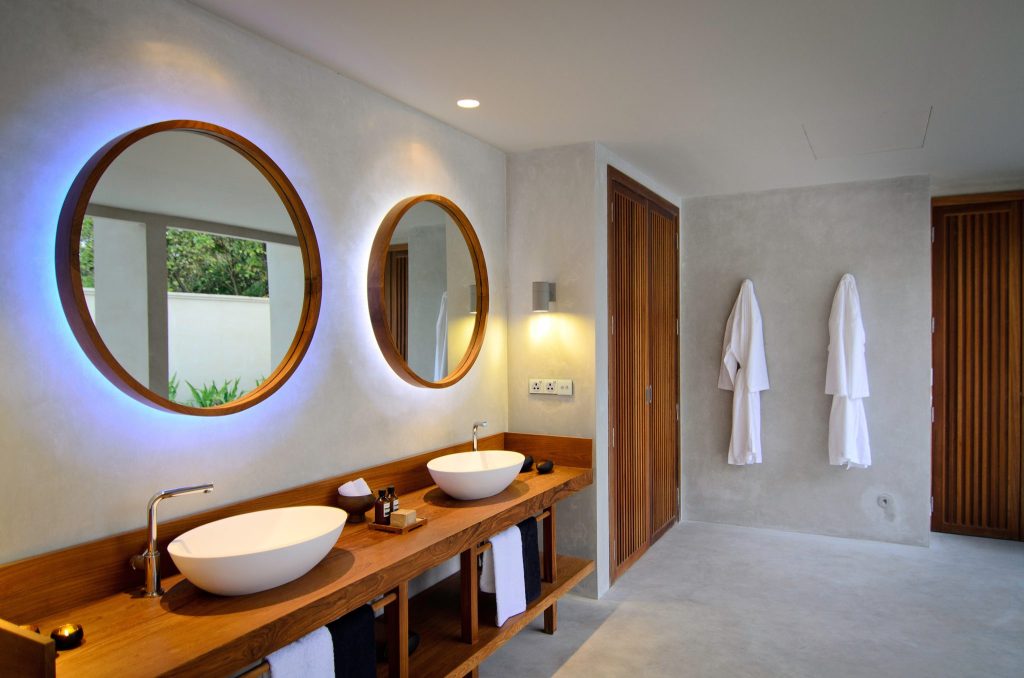 Modernes Badezimmer im Amilla Maldives mit zwei runden Spiegeln, weißen Waschbecken und hölzerner Waschtischplatte