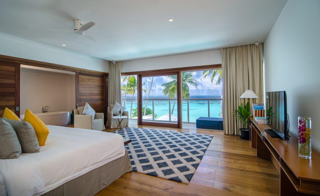 Geräumiges Great Beach Residence Zimmer im Amilla Maldives mit Bett, Badewanne, blau-weißem Teppich und Balkon zum Meer