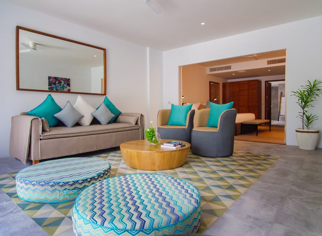 Modernes Wohnzimmer der Amilla Maldives Two Bedroom Beach Pool Villa mit Sofa, Sesseln, Holztisch und Schlafzimmer.