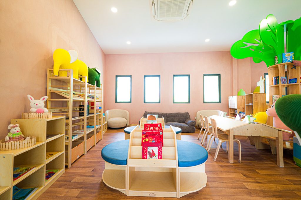 Heller Kids Club mit rosafarbenen Wänden, Holzregalen, blauen Sitzpolstern und vier Fenstern im ananea Madivaru Maldives