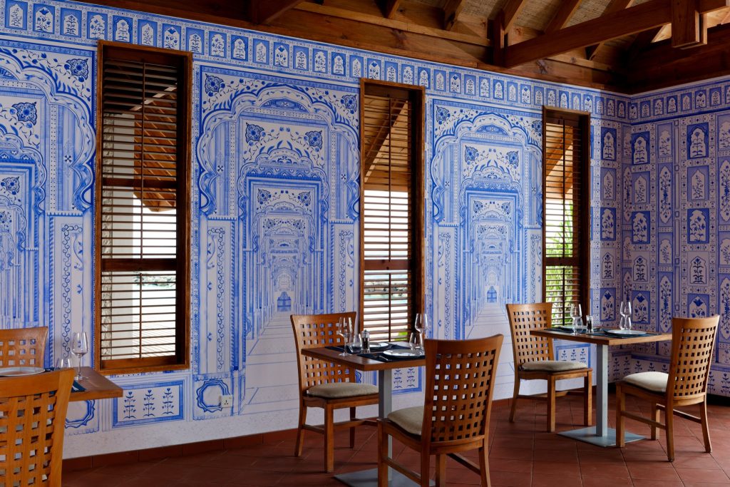 Restaurantraum mit blauen symmetrischen Mustern auf weißen Wänden, roten Fliesenboden und Holzdecke im ananea Madivaru.