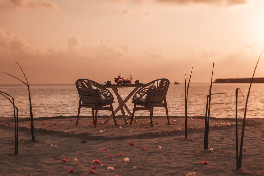Holztisch und geflochtene Stühle für zwei Personen am Strand bei Sonnenuntergang auf den