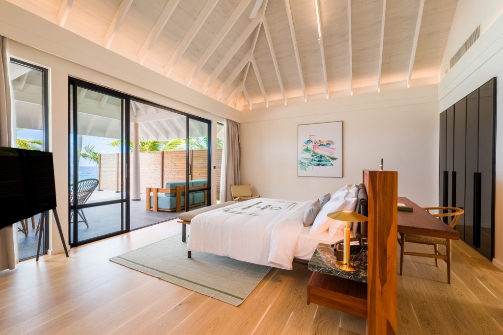 Zimmer der 2BR Beach Residence mit großem Bett, weißer Bettwäsche, Marmortisch und Terrasse mit Holzmöbeln