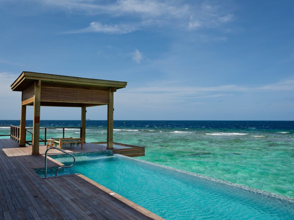 Terrasse mit rechteckigem Infinity-Pool aus Holz und Fliesen am Meer mit Holzpavillon und Tisch mit zwei Stühlen