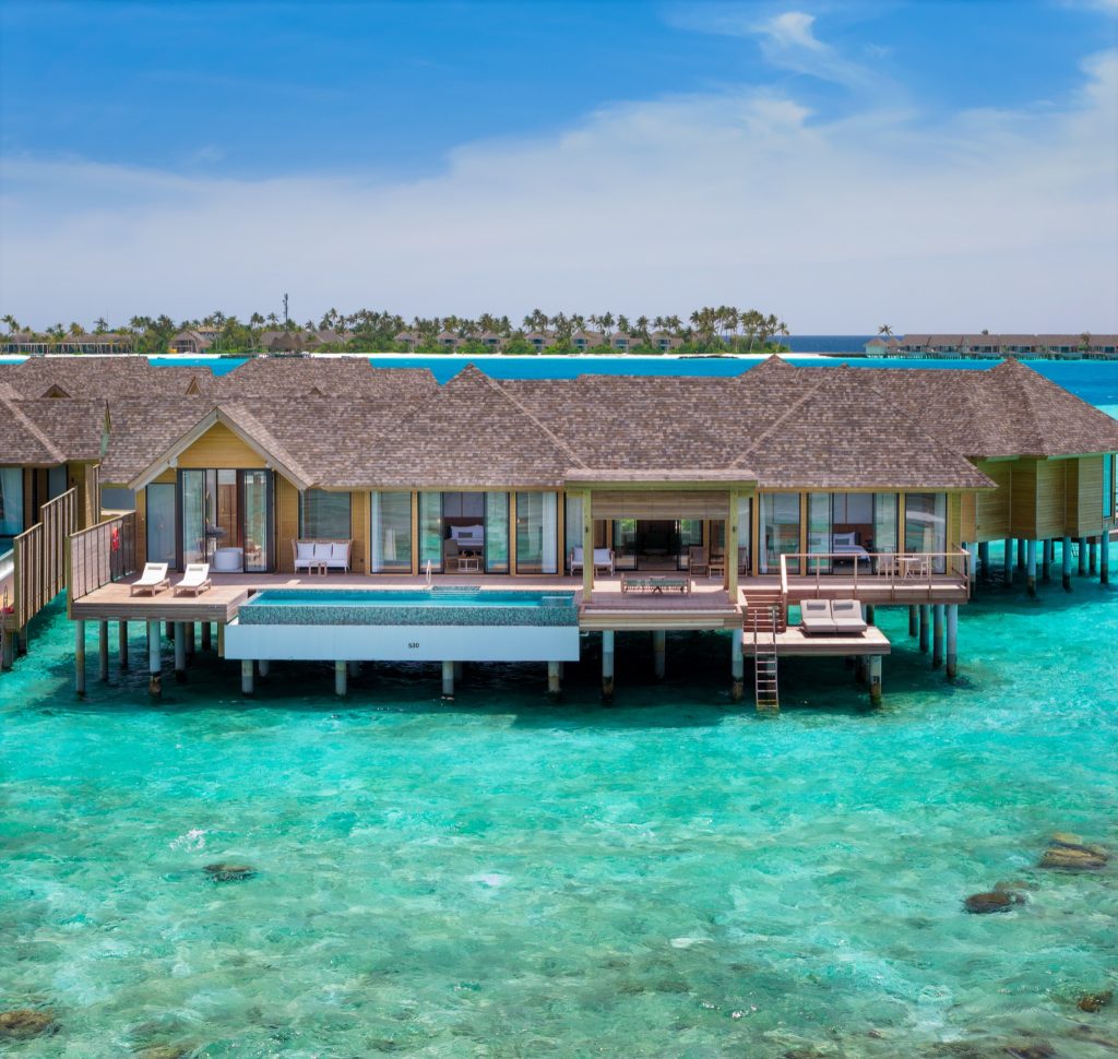 2BR Water Residence auf Stelzen über türkisfarbener Lagune mit Holz- und Glasarchitektur, Pool und See, frontal von oben