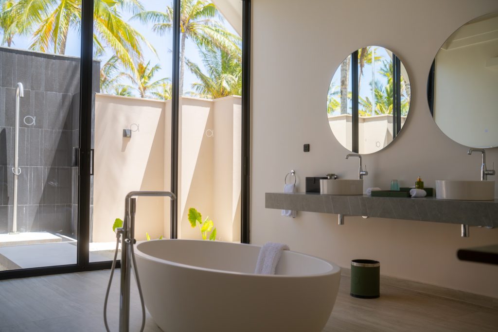 Modernes Badezimmer mit freistehender Badewanne, Doppelwaschtisch und Glasfront mit Blick auf Palmen