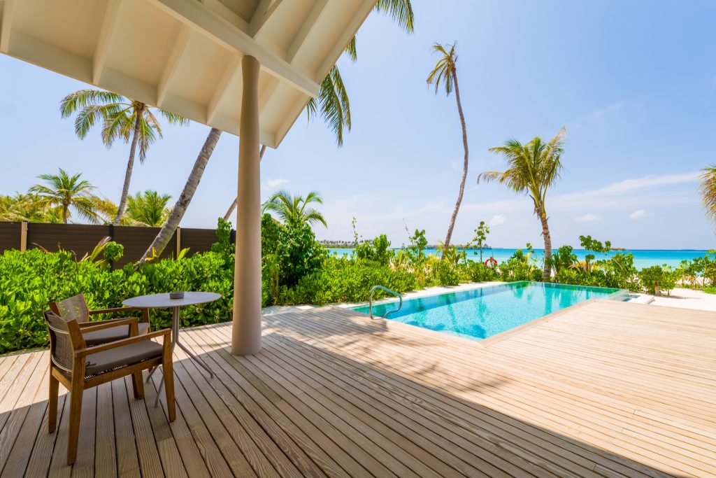 Terrasse mit Holzfußboden, rundem Tisch, Stuhl, kleinem Pool und Meerblick, umgeben von grüner Vegetation auf den