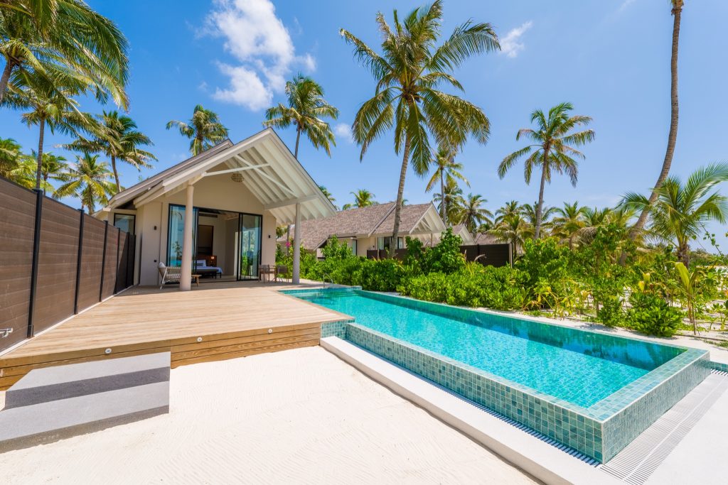 Beach Pool Villa mit großen Glasfenstern, Holzterrasse und türkisfliesen Pool in tropischer Umgebung auf den