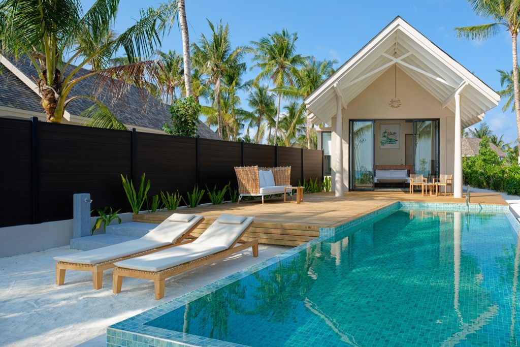 Poolvilla ananea Madivaru Maldives mit rechteckigem Pool, zwei Holzliegestühlen und Glasfronten im Bungalow