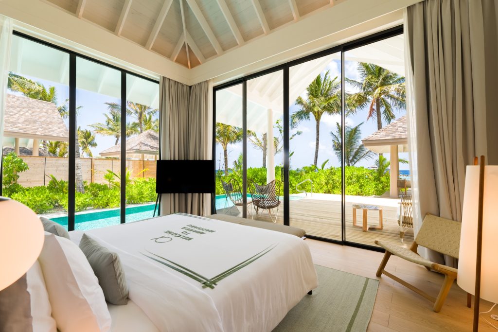 Modernes Hotelzimmer Deluxe Beach Pool Villa mit großem Bett, bodentiefen Fenstern und Terrasse mit Pool und Palmen
