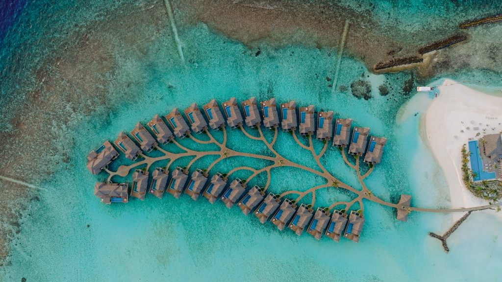 Luftaufnahme der Deluxe Water Pool Villas mit blauen Dächern und Holzelementen über türkisfarbenem Wasser
