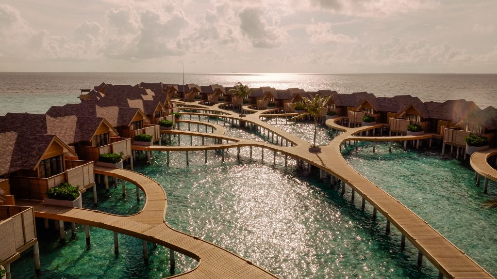 Überwasserbungalows der deluxe water pool villa mit Holzstegen über türkisfarbenem Meer bei Abenddämmerung