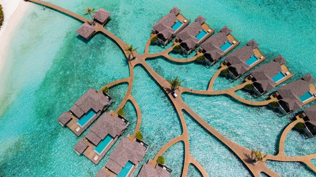 Luftaufnahme von überwasser Water Pool Villas mit strohgedeckten Dächern und hölzernen Stegen auf türkisfarbenem Wasser