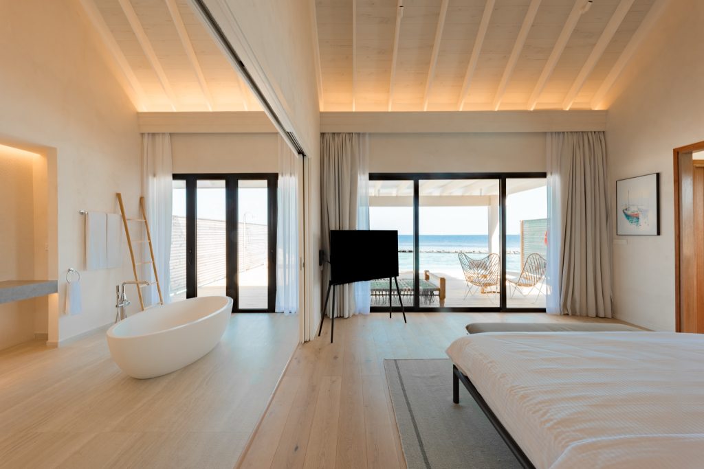 Modernes Zimmer der Water Pool Villa mit freistehender Badewanne, Glas-Schiebetüren und Blick auf das Meer