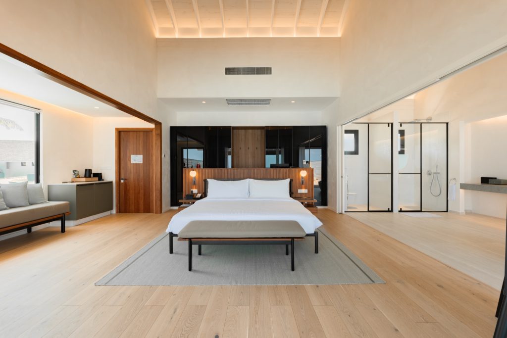 Geräumiges Water Pool Villa Zimmer mit großem Bett, weißer Bettwäsche, Holzboden und gläsernem Badezimmer auf den