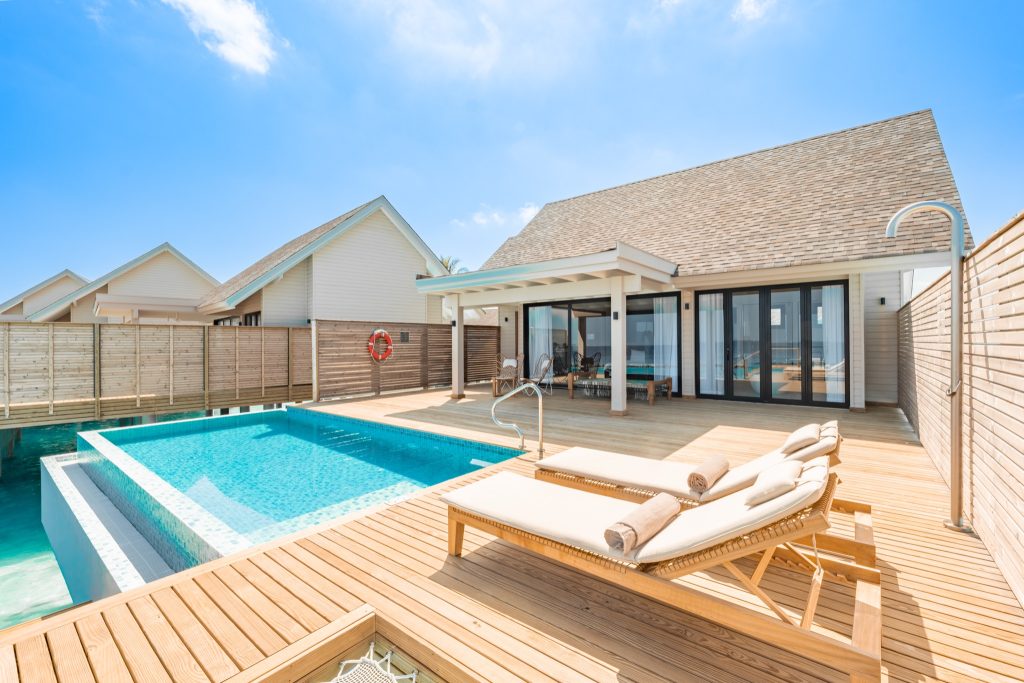 Terrasse einer Water Pool Villa mit Holzliegen, privatem Pool und Bungalow mit großen Glasfenstern in den