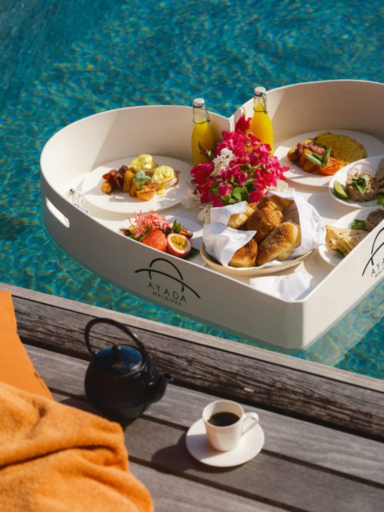 Herzförmiges Tablett mit Frühstück, Gebäck, Früchten und Getränken auf blauem Poolwasser bei Ayada Maldives