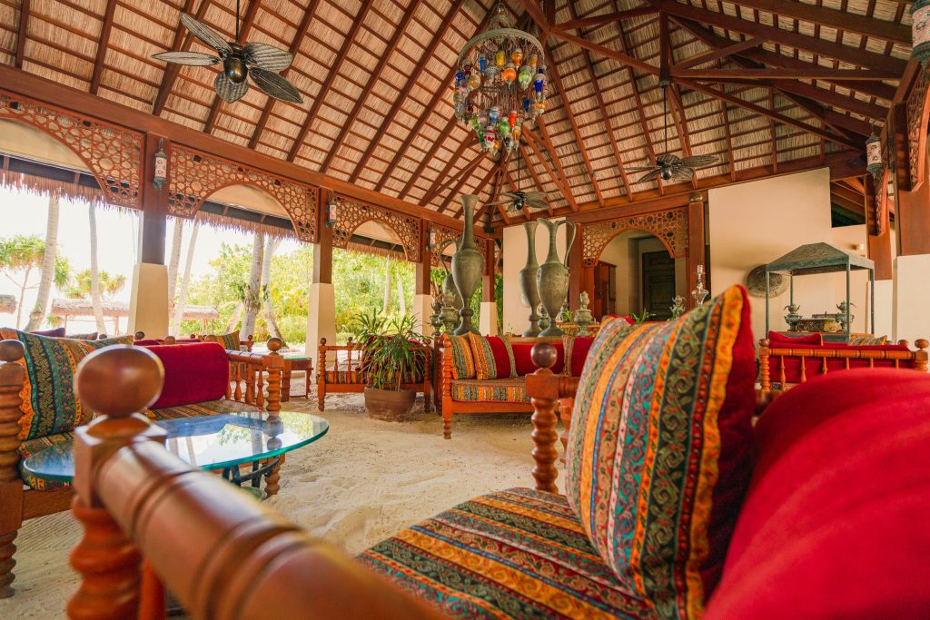 Offene Ottoman Lounge mit Holzmöbeln, bunten Kissen, Glas-Couchtischen und Palmdach bei Ayada Maldives