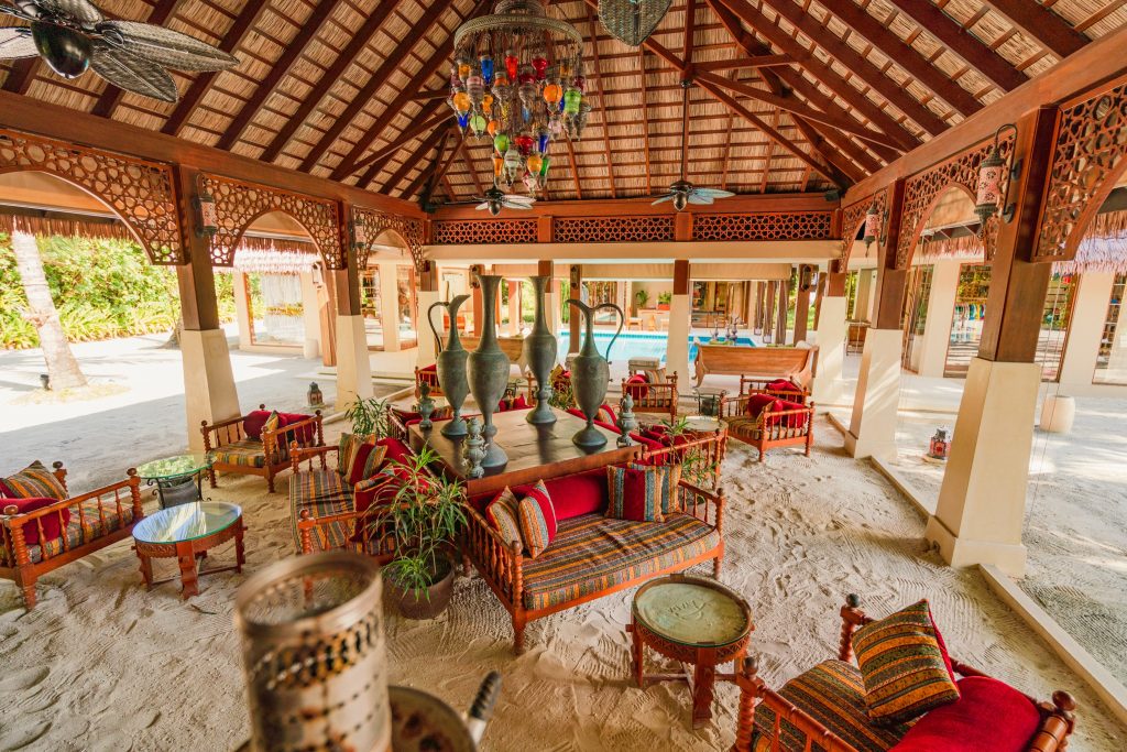 Offene Bar Ottoman Lounge im Ayada Maldives mit Holzmöbeln, bunten Polstern und großen Metallvasen auf einem Holztisch