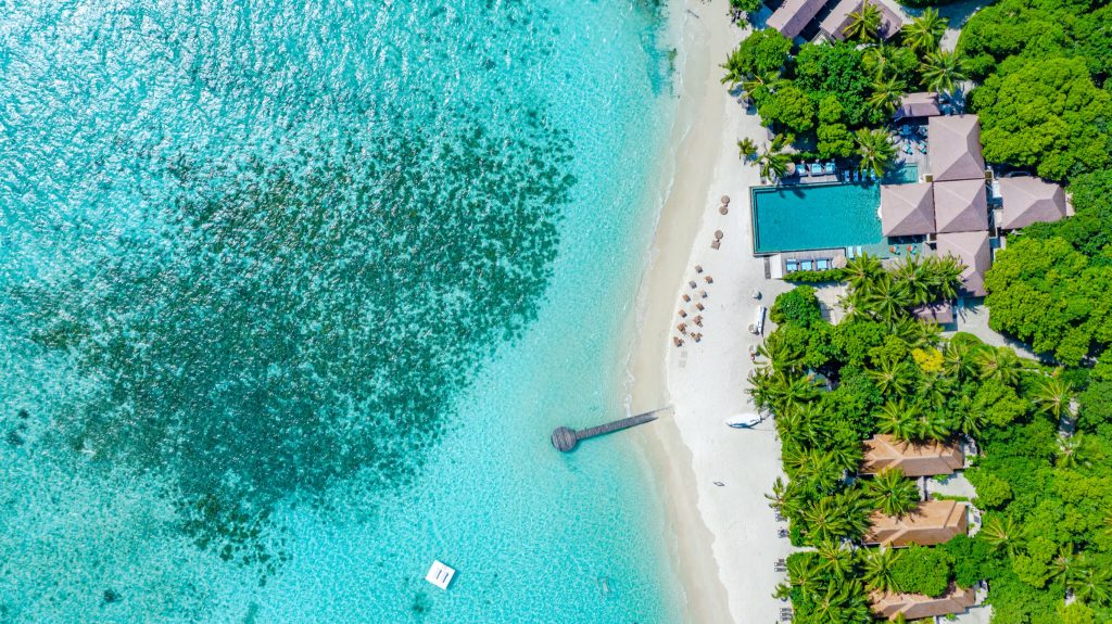 Vogelperspektive auf Bar Zero Degree mit Holzsteg, Swimmingpool, Liegestühlen und Palmen an einem Malediven-Strand