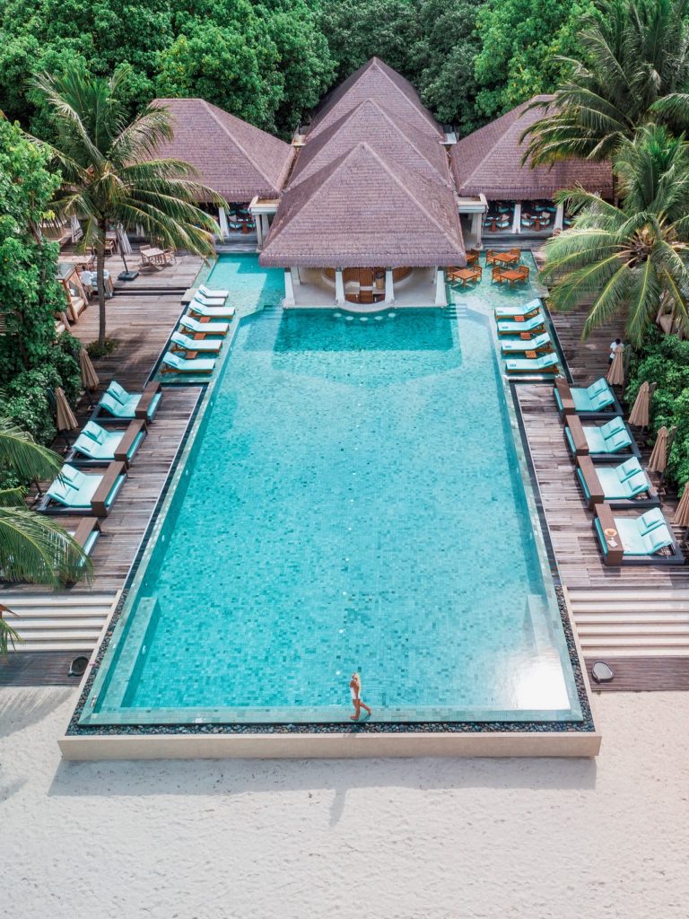 Luftaufnahme der Bar Zero Degree mit großem rechteckigem Pool, blauen Liegen und Schilfdächern in Ayada Maldives