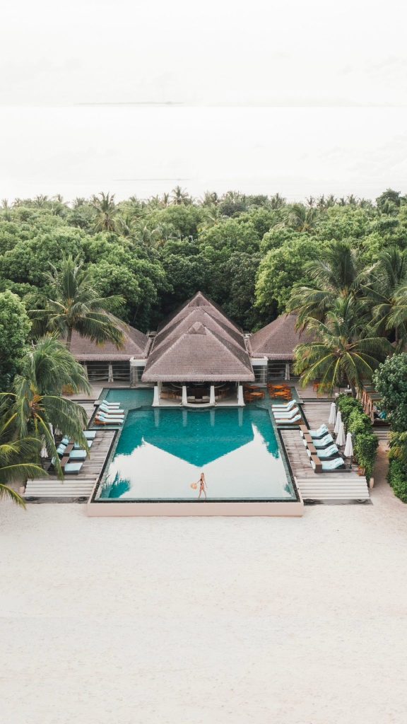 Großer rechteckiger Pool mit klarem blauem Wasser, umgeben von Holzdecks und tropischer Vegetation im Ayada Maldives