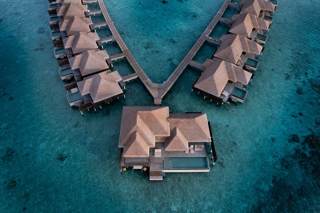 Wasserbungalows auf Stelzen mit braunen Dächern und hölzernem Steg über blauem Ozean, Luftaufnahme Ayada Maldives
