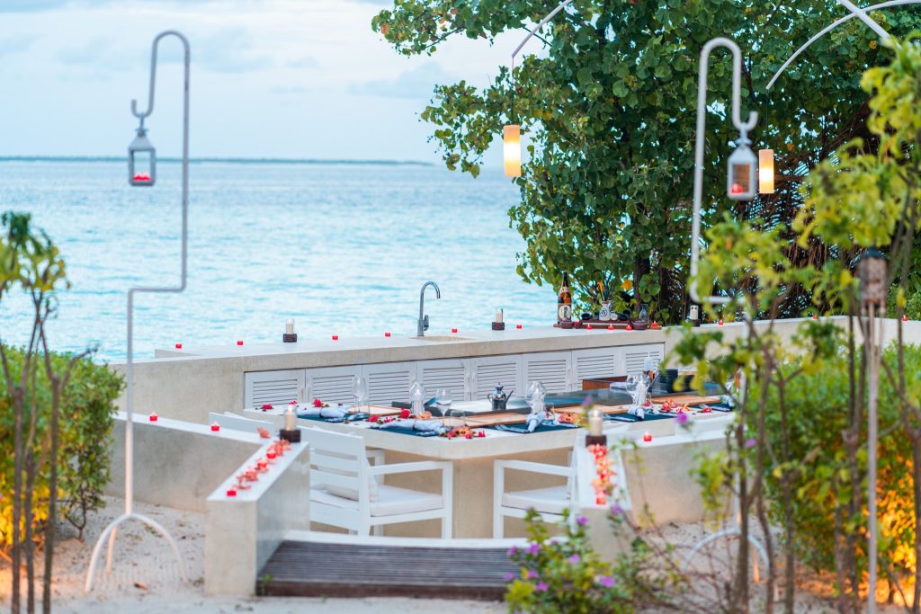Outdoor-Restaurant Mizu mit weiß gestrichenen Holzmöbeln, dunkelblauen Tischläufern und Kerzen am Abend auf den