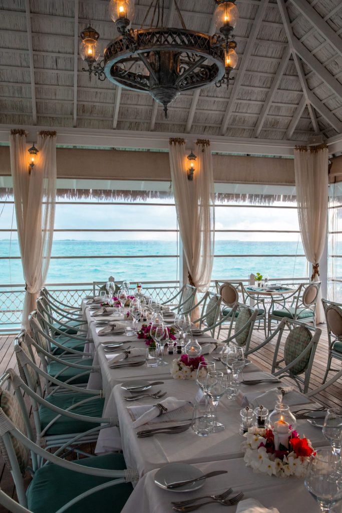 Tisch mit weißen Tischdecken, Kristallgläsern und Blumengestecken im Restaurant Ocean Breeze mit Meerblick