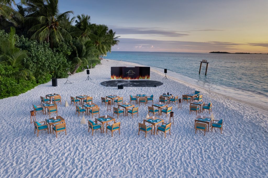 Offener Strandbereich mit Holztischen und hellblauen Sitzkissen am Meer im Restaurant Sea Salt Ayada Maldives