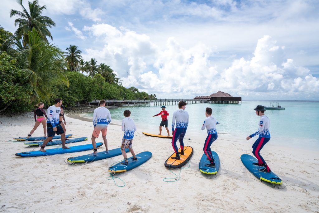 Gruppe auf Surfbrettern am Strand von Ayada Maldives, Palmen und Holzbungalows im Hintergrund