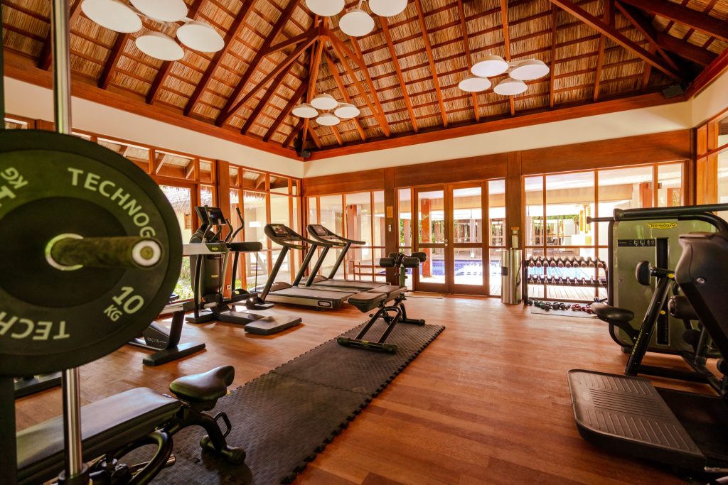 Fitnessraum im Ayada Maldives mit Laufbändern, Gewichten und großen Fenstern zum Poolbereich