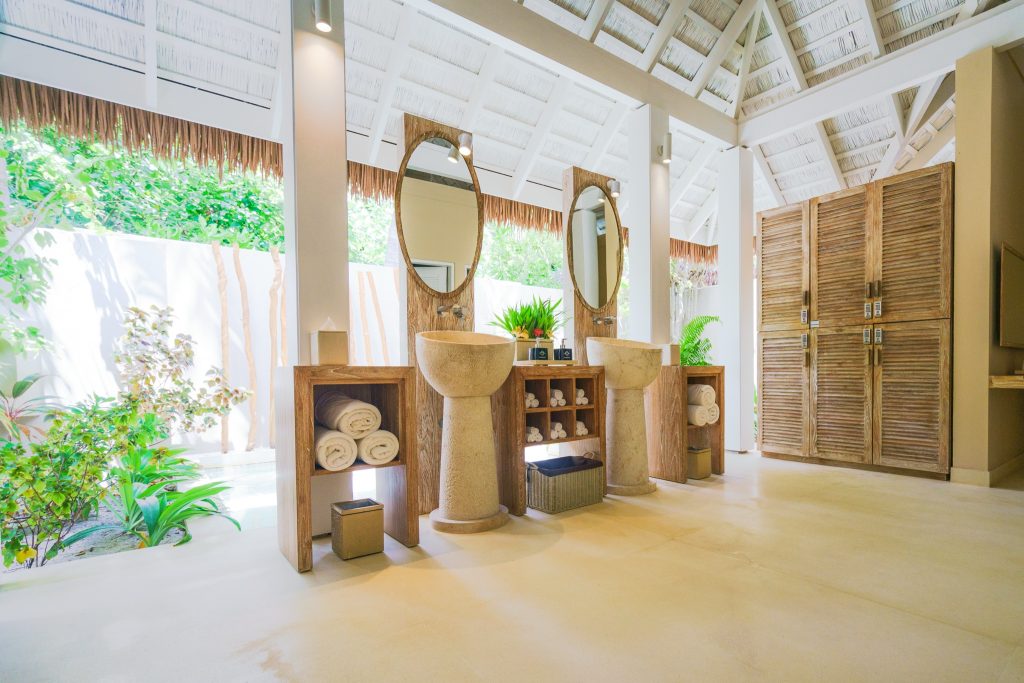 Badezimmer mit zwei ovalen Spiegeln in Holzrahmen, freistehenden Steinwaschbecken und Holzregalen mit Handtüchern